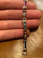 Close-up view of the bracelet links showcasing baguette-cut rubies, emeralds, sapphires, and clear stones in gold overlay with sterling silver.