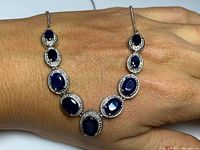 Front view of necklace displaying oval sapphires surrounded by diamonds against skin.