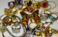 Collection of costume jewelry laid out including rings, brooches, bracelets and necklaces with colorful stones and gold-tone metal.