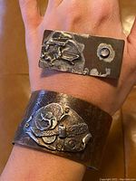 Photo showing the rectangular sterling silver brooch with abstract design and inset stone alongside the wide hammered copper cuff bracelet worn on wrist.
