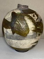 Front view of round, abstract decorated Raku pottery vase with multi-tone earthy colors and textured surface.