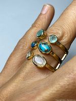 Ring worn on finger showing six gemstones with gold bezels and silver bands.