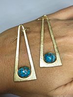 Pair of modernist 14K gold triangular earrings with oval Kingsman turquoise stones displayed on a hand, showing front and side views.