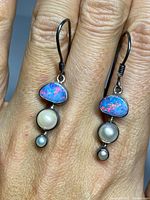 Front view of both earrings held in hand to show size and detail of opal and pearls.