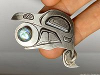 Close-up of the sterling silver pendant with abalone inlay showing Northwest Coast indigenous art 'Transformation' motif and surface wear.