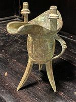 Angled front view of the bronze vessel showing legs, spout, handle, and surface wear.