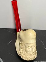Front view of antique meerschaum smoking pipe carved with a bearded man's face and red amber stem.