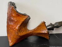 Close-up of carved burl wood pipe bowl with textured black rim and attached black bakelite stem, showcasing the wood grain and stem design.