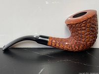 Side profile of antique briar wood smoking pipe with textured pebble grain design and curved black stem against neutral background.