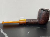Side view of antique burl wood pipe with amber-colored stem on black surface