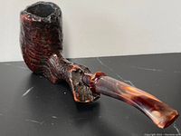 Full view of antique burl wood smoking pipe showing textured bowl and amber curved stem on black surface.