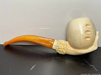 Side view of antique meerschaum and amber pipe showing hand-carved hand holding bowl, floral carvings, and amber stem.