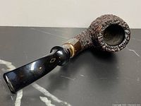 Side view of antique tobacco pipe with burl wood bowl and sterling silver stem connection on black surface.