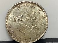 Obverse side of 1962 Canadian silver dollar featuring two voyageurs in a canoe with detailed design and inscription.