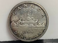 Reverse side of the 1965 Canadian silver dollar featuring a canoe with two men paddling and the text 'CANADA DOLLAR 1965'.