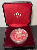 Front view of the silver dollar in original black case with red velvet interior and silver maple leaf emblem.