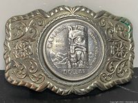 Front view of belt buckle showing the central 1958 Canadian silver dollar coin featuring a totem design and surrounding engraved floral metal backing.