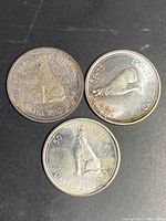 Reverse sides of three Canadian silver half dollar centennial coins showing commemorative designs including a howling wolf and a maple leaf.