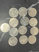 Photo showing 13 Canadian dollar coins with various designs including the British Columbia Centennial and 1956 canoe design on black surface.