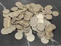 Pile of Canadian five-cent nickels on a dark marble surface, showing a mix of worn and cleaner coins.