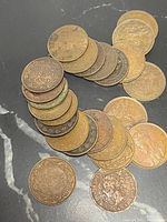 24 assorted early British half penny coins arranged on black surface. Various ages and wear levels visible.