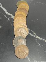 Group of 20 British pennies arranged in a line showing a side view with visible monarch portraits on some coins.