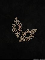 Pair of delicate antique brass findings shown separately on black background, highlighting their intricate deco design and scroll details.