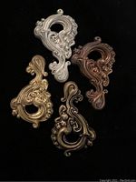 Four antique ornate metal findings in gold, silver, bronze, and copper tones, showing front detail and hollow back design.