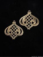 Two antique brass decorative findings shown on black background highlighting lattice and scrollwork pattern, one upright and one inverted.