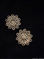 Two antique brass daisy-shaped findings showing detailed filigree work and cut patterns.