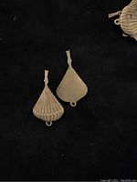Two brass balloon or shell shaped findings shown against black background, with one showing front ridged side and the other showing smooth backside.