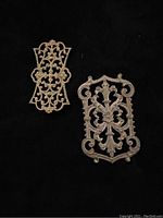 Two large, ornate brass metal findings with intricate openwork patterns on a dark background.