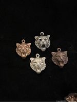 Four different lion head pendants shown on black background to display detail and colors in brass and mixed alloys.