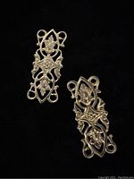 Two antique brass filigree findings shown on a black background, displaying detailed leaf and scroll design with several connection loops.