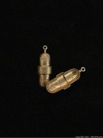Two brass deco pendant findings shown side by side on black background, highlighting capsule shape and decorative design.