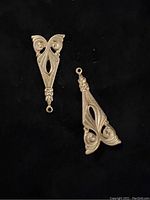 Two ornate antique brass jewelry findings shown from front on black background, displaying detailed scrollwork and closed jump rings at top.