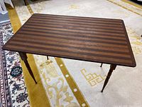 View of the full table showing wooden striped top and turned legs on carpet.