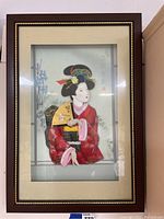 Full view of the shadow box wall art featuring the geisha figure in red kimono behind glass with wooden frame.