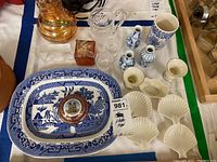 Photo showing Blue Willow platter, Lenox shell-shaped candlestick holders, Belleek dish, three blue bud vases, clear glass canister, and several paperweights including one chipped.