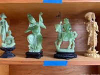 Four resin Chinese statues displayed on a wooden shelf showing variety in pose, color, and base style