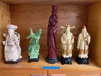 Set of five Chinese resin statues on wooden shelving, showing all items in the lot