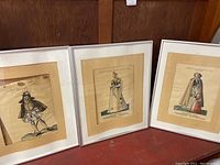 Photo showing three framed European nobility fashion illustrations, side by side, with varied historical clothing styles.