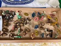 Wide shot showing assortment of floral and bow decorative thumb tacks with metal holders on wooden tray.