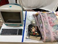 Shows the full lot with vintage Apple iMac G3, keyboard, mouse, software disks, and folded pastel bedspread.