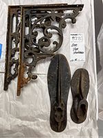 Two iron shelf holders stacked, one pair of iron shoe stretchers, one adult size and one child size with visible rust and wear.