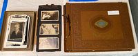 Overall lot showing box of loose prints, a black photo album page with mounted photographs, and the closed photo album with embossed cover