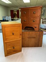 Three wooden storage boxes including one light wood apothecary chest with drawers and two smaller oak wood boxes stacked on a table indoors.