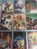 Photo showing nine fantasy art trading cards laid out in a 3x3 grid, depicting various fantasy scenes with muscular figures, horses, mythical creatures, and dramatic landscapes.