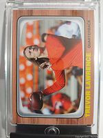 Front view of the 2021 Topps Trevor Lawrence Rookie Card encased in hard acrylic protector, showing wood grain border and bright yellow player name and position text.