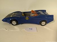 Side view of blue 1984 Kenner Batmobile showing overall shape, Batman logo on side, white bat emblem on wheels, and transparent orange windshield canopy.